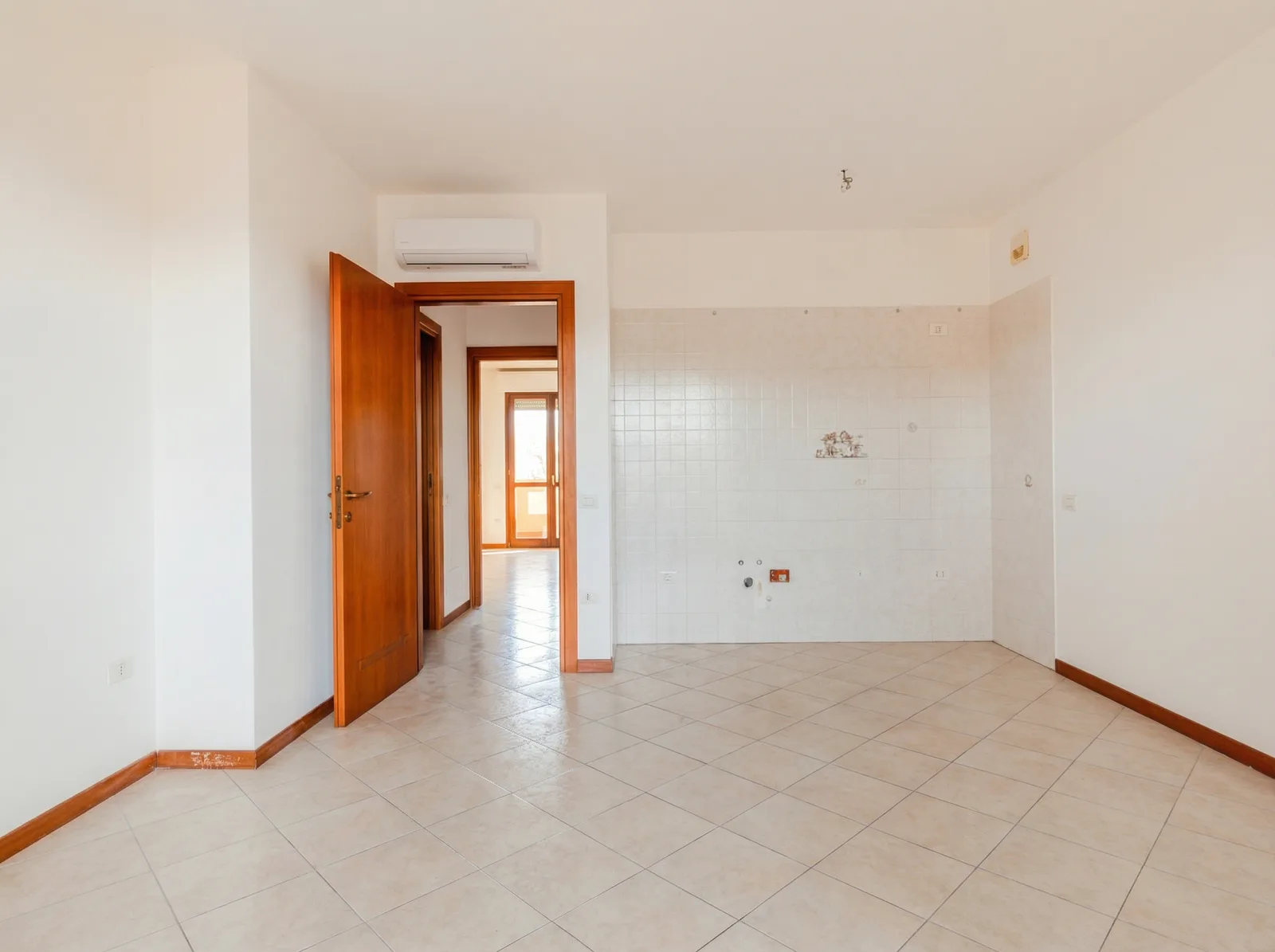 Angolo cucina e soggiorno vuoto e lo stesso ambiente arredato in stile moderno, con isola e divano in pelle: Prima